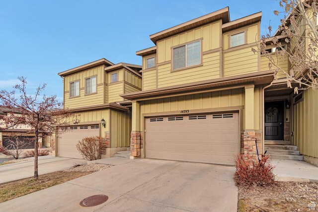 multi unit property with stone siding, a garage, board and batten siding, and concrete driveway