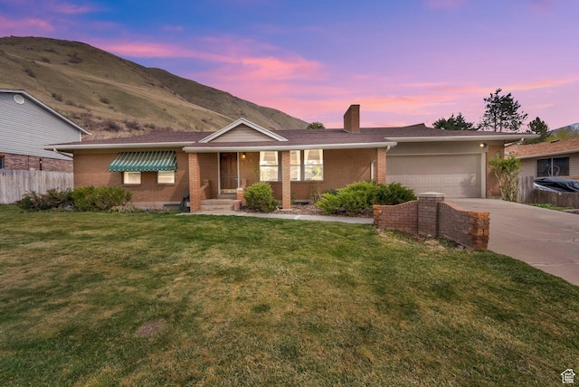 ranch-style home with driveway, an attached garage, fence, brick siding, and a yard
