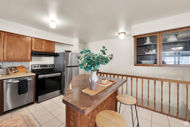 276 N 1100 E, Springville, UT 84663 - kitchen featuring light tile patterned floors, stainless steel appliances, under cabinet range hood, a breakfast bar, and brown cabinetry