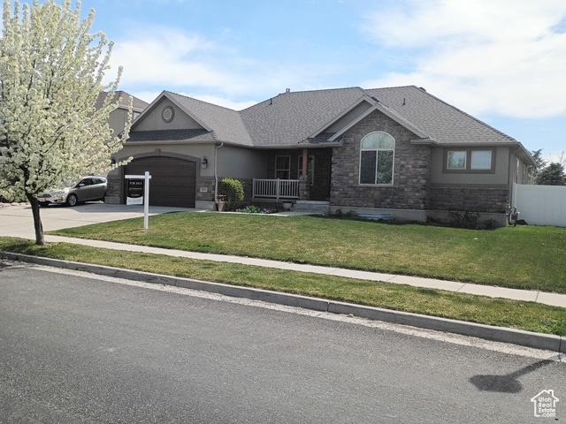 single story home with a garage, stone siding, fence, a front lawn, and driveway