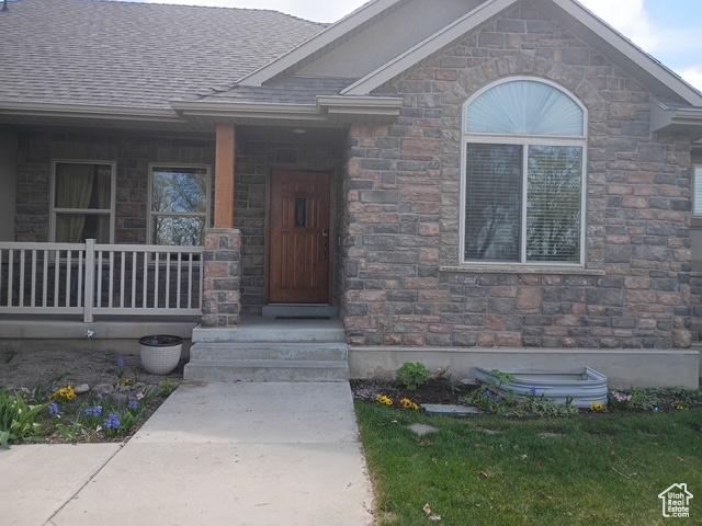 property entrance with roof with shingles, stone siding, and covered porch