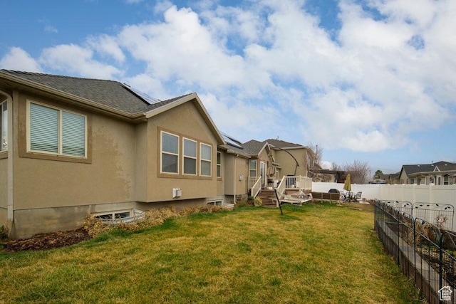 view of side of property with a deck, solar panels, a yard, a fenced backyard, and stucco siding