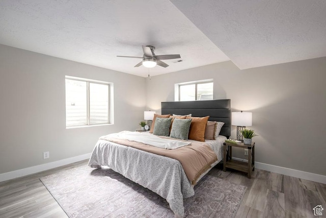 bedroom with visible vents, baseboards, a textured ceiling, and wood finished floors