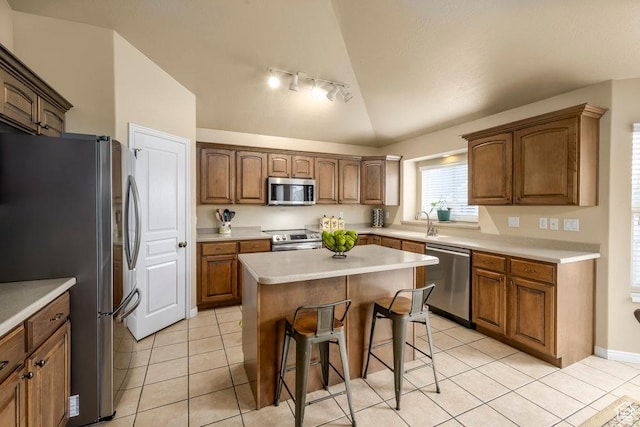 kitchen with light tile patterned floors, track lighting, vaulted ceiling, stainless steel appliances, and a breakfast bar area