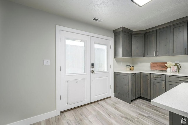 interior space featuring light wood-style floors, a textured ceiling, baseboards, and visible vents