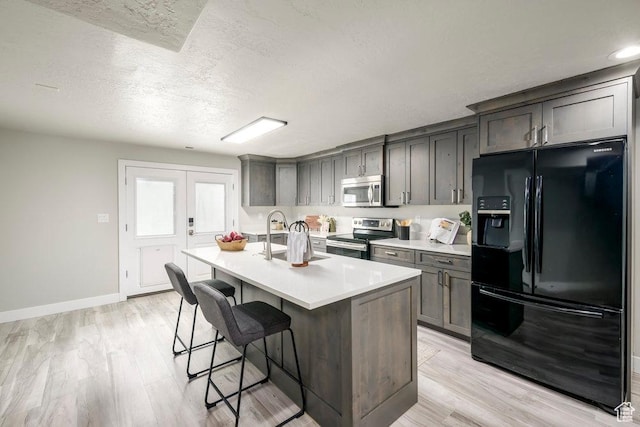 kitchen featuring a sink, light countertops, appliances with stainless steel finishes, a kitchen breakfast bar, and a center island with sink