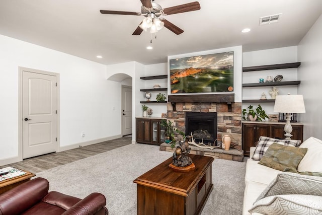 living area with visible vents, a ceiling fan, a fireplace, baseboards, and arched walkways