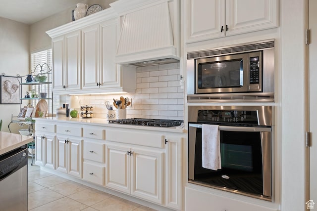 2653 Rio Lobo Dr, St George, UT 84770 - kitchen with white cabinetry, tasteful backsplash, custom exhaust hood, light tile patterned floors, and stainless steel appliances