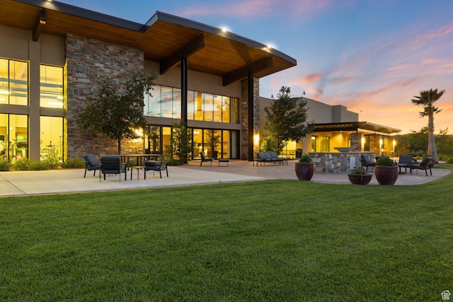 714 N Millcreek Springs Dr, Washington, UT 84780 - back of property at dusk featuring stone siding, a patio area, and a lawn