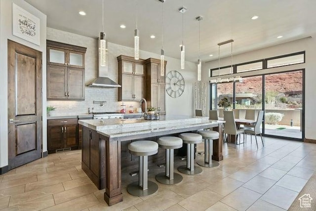 3052 N Snow Canyon Pkwy Unit 36, St George, UT 84770 - kitchen with backsplash, light stone countertops, a breakfast bar, wall chimney range hood, and a kitchen island with sink