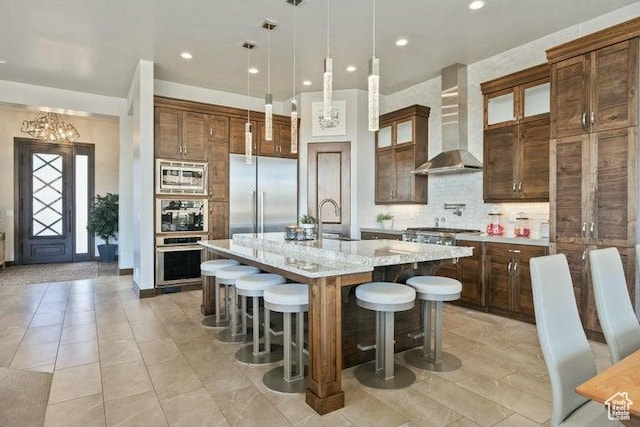 3052 N Snow Canyon Pkwy Unit 36, St George, UT 84770 - kitchen featuring wall chimney exhaust hood, tasteful backsplash, an island with sink, a breakfast bar area, and built in appliances