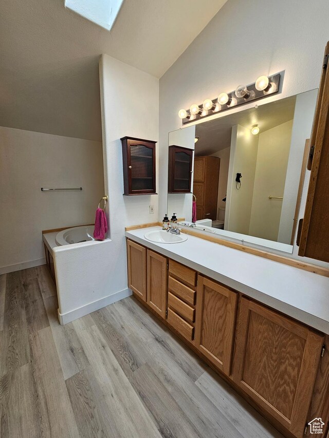 2350 S Red Creek Rd, Fruitland, UT 84027 - full bath with vanity, baseboards, vaulted ceiling with skylight, a garden tub, and wood finished floors