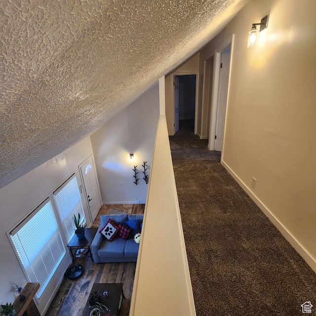 corridor with baseboards, lofted ceiling, carpet flooring, and a textured ceiling