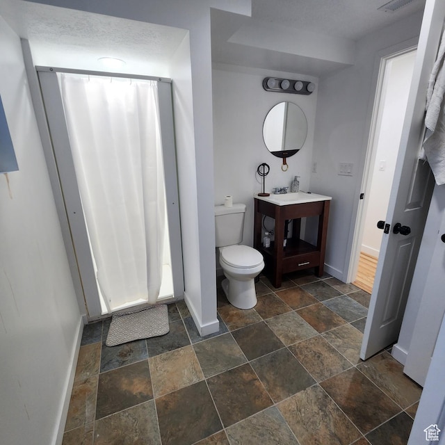 bathroom featuring baseboards, toilet, stone finish floor, and vanity