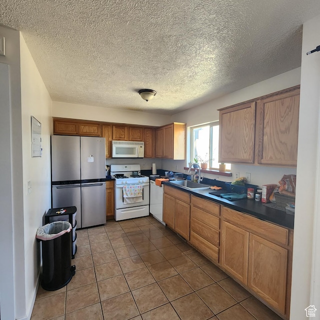 kitchen with a textured ceiling, white appliances, dark countertops, a sink, and light tile patterned floors