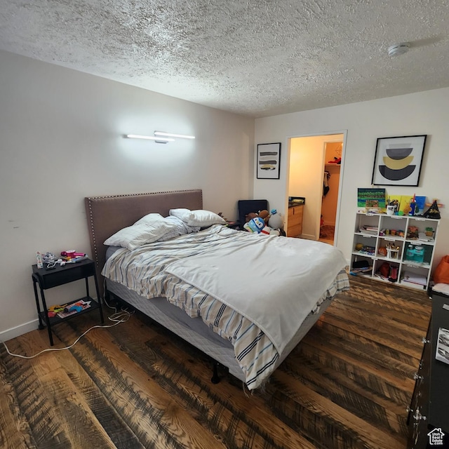 bedroom with a spacious closet, a textured ceiling, a closet, and wood finished floors