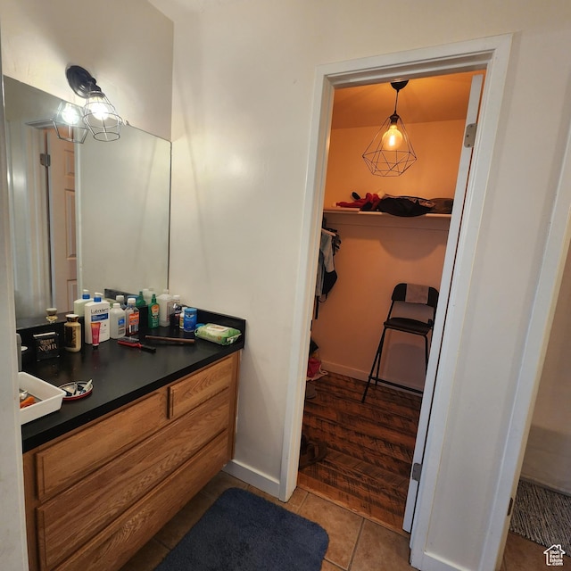 bathroom with tile patterned floors, vanity, a walk in closet, and baseboards