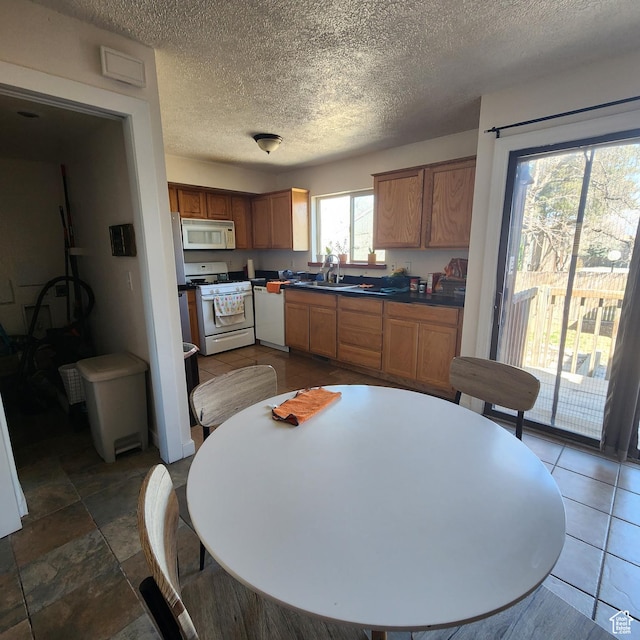kitchen featuring white appliances, dark countertops, brown cabinets, and a sink