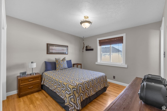 bedroom featuring light wood finished floors, baseboards, and a textured ceiling