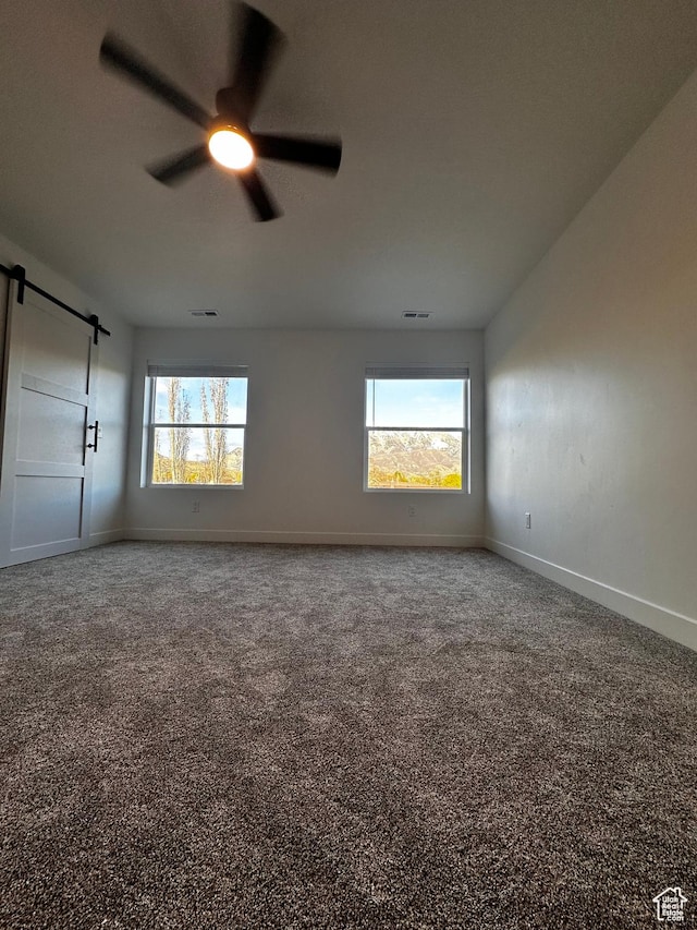 unfurnished room featuring a wealth of natural light, a barn door, a ceiling fan, and baseboards