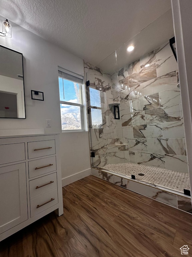 full bathroom with wood finished floors, vanity, baseboards, a marble finish shower, and a textured ceiling