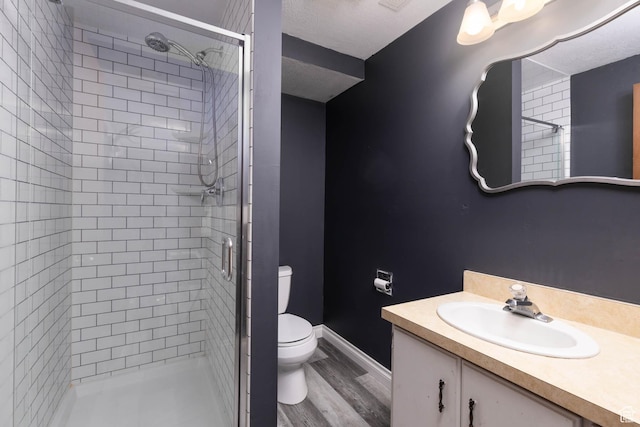 full bath featuring toilet, vanity, a shower stall, wood finished floors, and baseboards