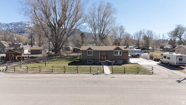 bi-level home featuring concrete driveway, a fenced front yard, a mountain view, and a front lawn
