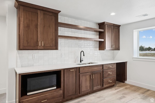kitchen with light countertops, tasteful backsplash, a sink, open shelves, and light wood-type flooring