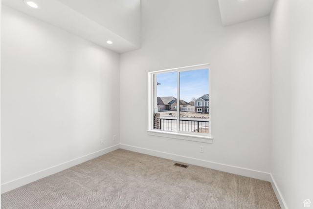 carpeted spare room featuring a towering ceiling, baseboards, visible vents, and recessed lighting