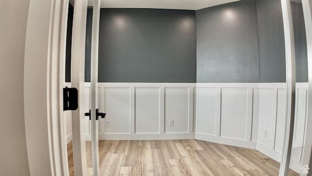 spare room with light wood-style flooring, a decorative wall, and a wainscoted wall
