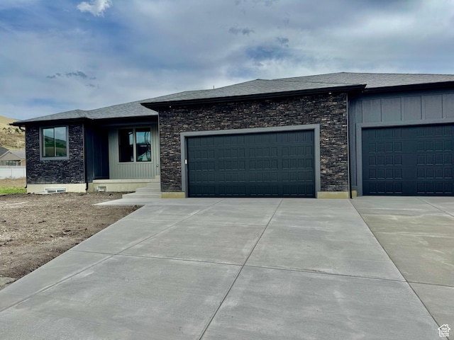 prairie-style home featuring concrete driveway, stone siding, an attached garage, and board and batten siding