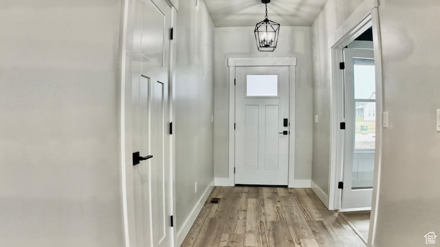 doorway featuring visible vents, baseboards, light wood-type flooring, and a chandelier