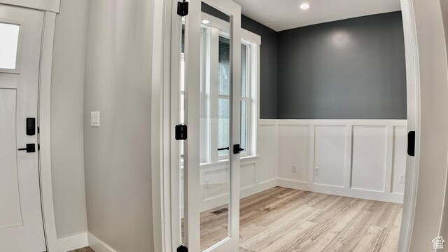 doorway with a decorative wall, a wainscoted wall, light wood-type flooring, and recessed lighting