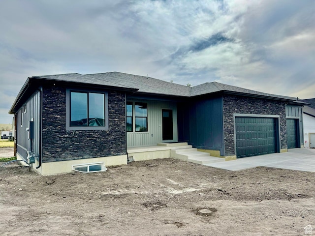 prairie-style house featuring an attached garage, driveway, and stone siding