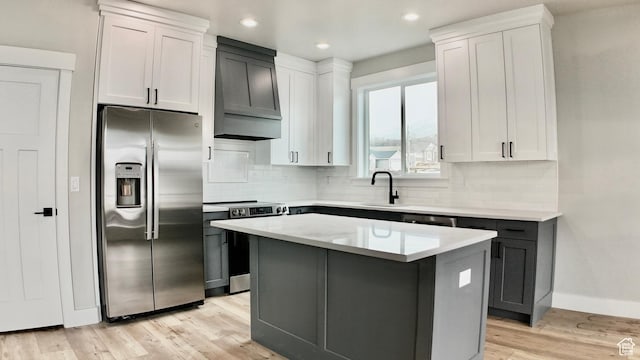 kitchen featuring light wood-style flooring, light countertops, stainless steel appliances, custom range hood, and backsplash