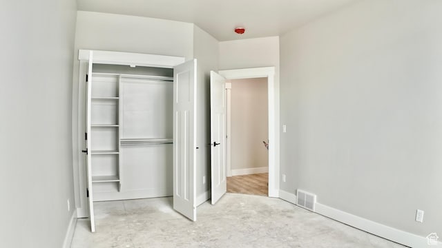 unfurnished bedroom with concrete floors, visible vents, baseboards, and a closet