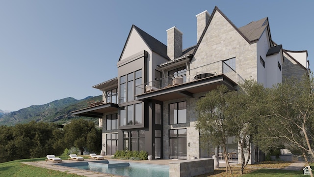 back of house featuring a balcony, a chimney, an outdoor pool, and a mountain view