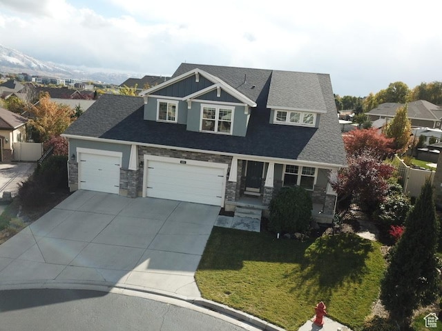 craftsman house featuring driveway, a front yard, stone siding, fence, and a garage
