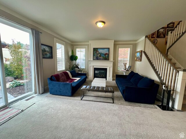 carpeted living area featuring a glass covered fireplace, crown molding, stairs, and visible vents