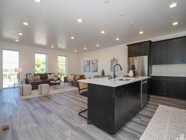 kitchen with an island with sink, light countertops, a sink, appliances with stainless steel finishes, and open floor plan