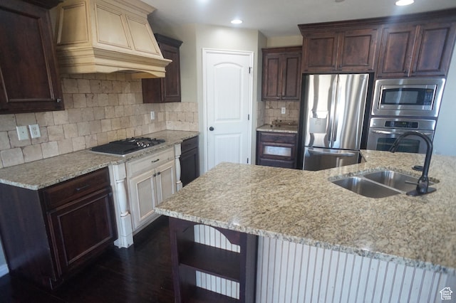 kitchen with premium range hood, backsplash, a sink, dark brown cabinets, and appliances with stainless steel finishes