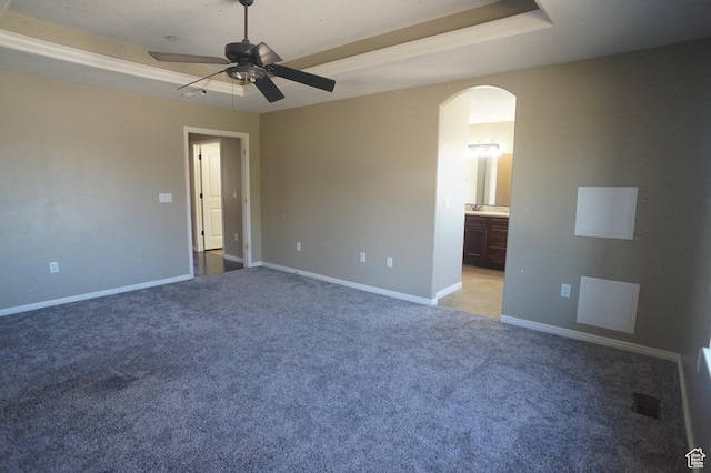 unfurnished bedroom with arched walkways, a tray ceiling, baseboards, and light colored carpet
