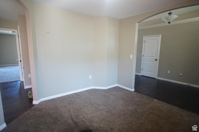 empty room featuring dark wood finished floors, baseboards, arched walkways, and dark colored carpet