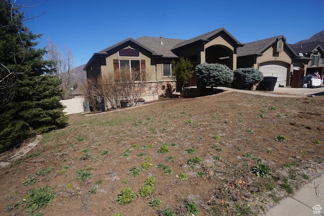 single story home featuring stone siding, roof with shingles, stucco siding, fence, and an attached garage