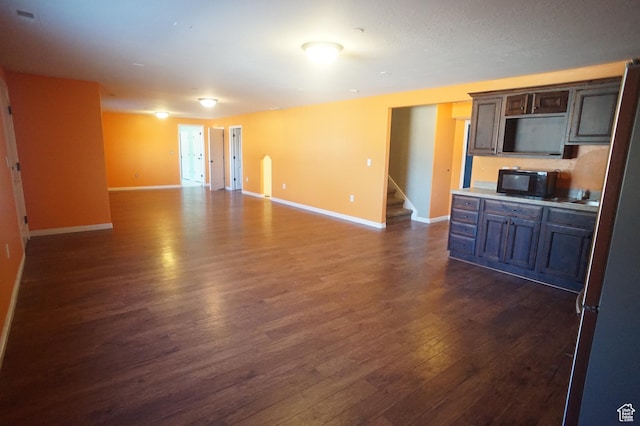 unfurnished living room with baseboards, dark wood-style flooring, and stairs