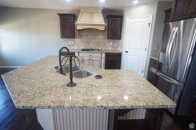kitchen featuring decorative backsplash, custom exhaust hood, stainless steel appliances, an island with sink, and a sink