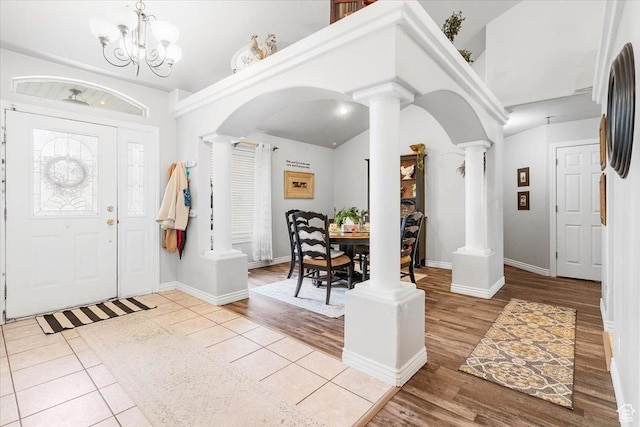 foyer featuring ornate columns, arched walkways, wood finished floors, and a notable chandelier