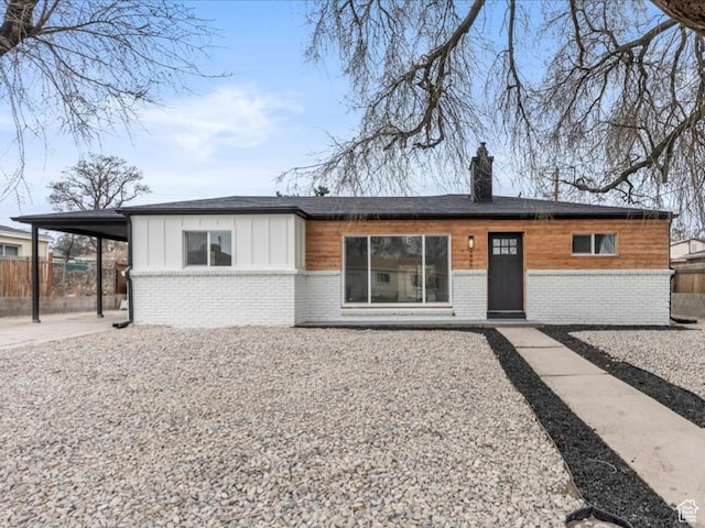 view of front of house featuring a chimney, fence, board and batten siding, brick siding, and a carport