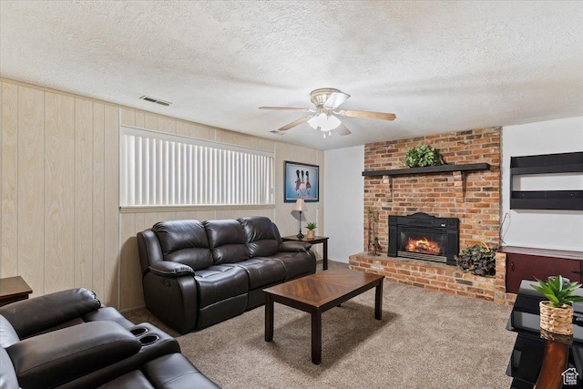 living room with carpet floors, a ceiling fan, a fireplace, a textured ceiling, and visible vents