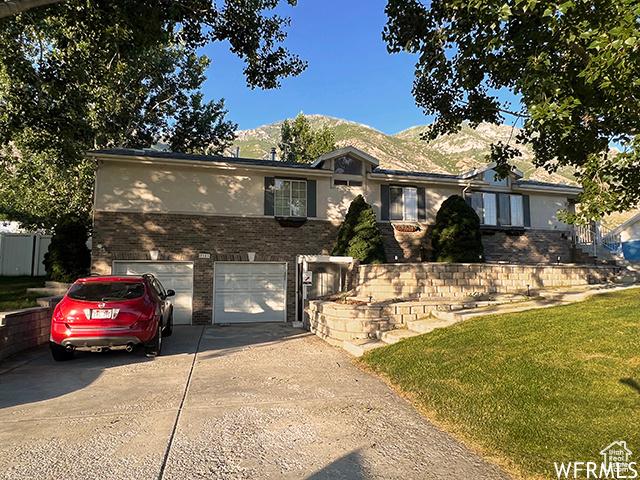 ranch-style home featuring a garage, concrete driveway, brick siding, stucco siding, and a mountain view